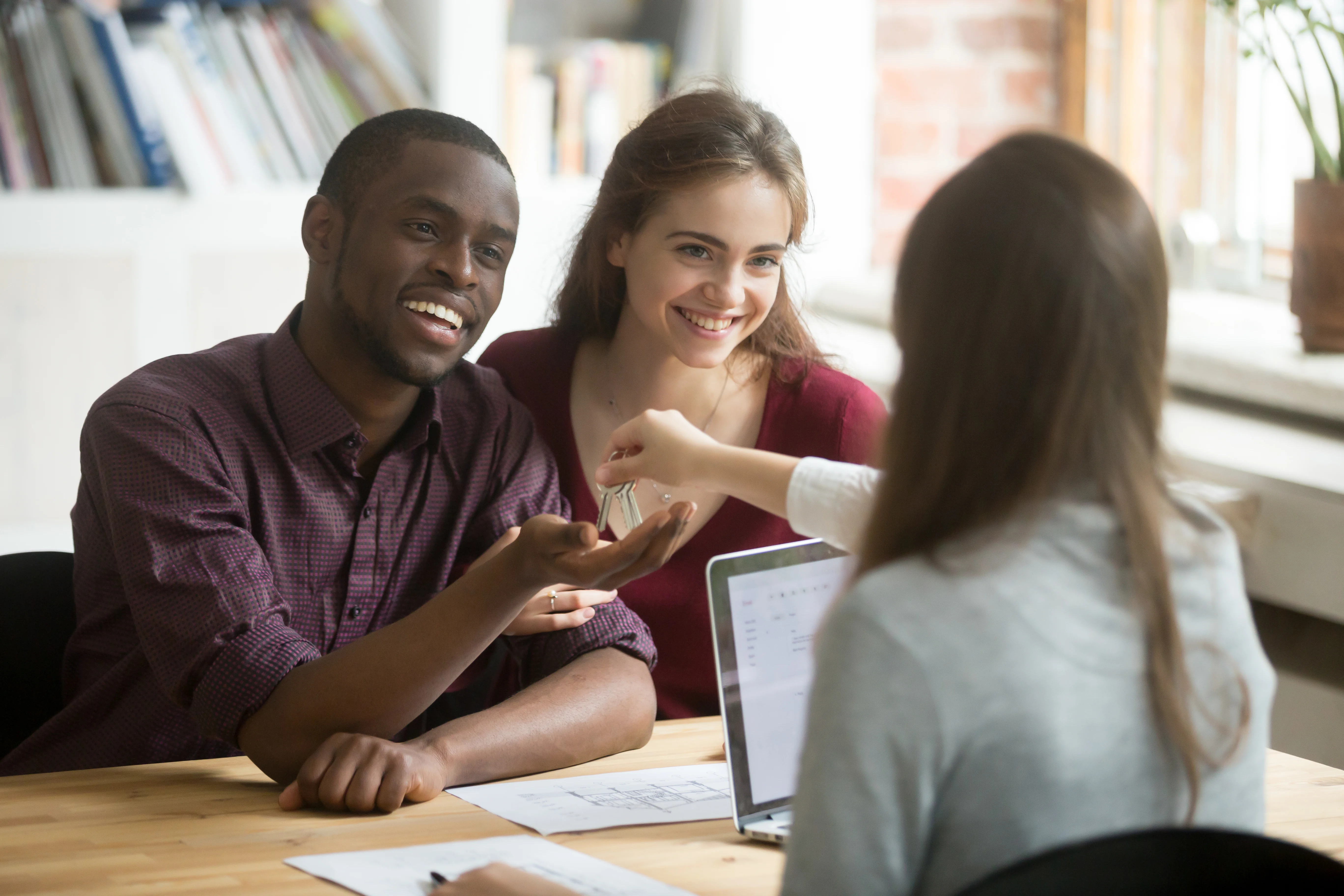 A joyful meeting with a couple smiling at a table while receiving keys from a woman.