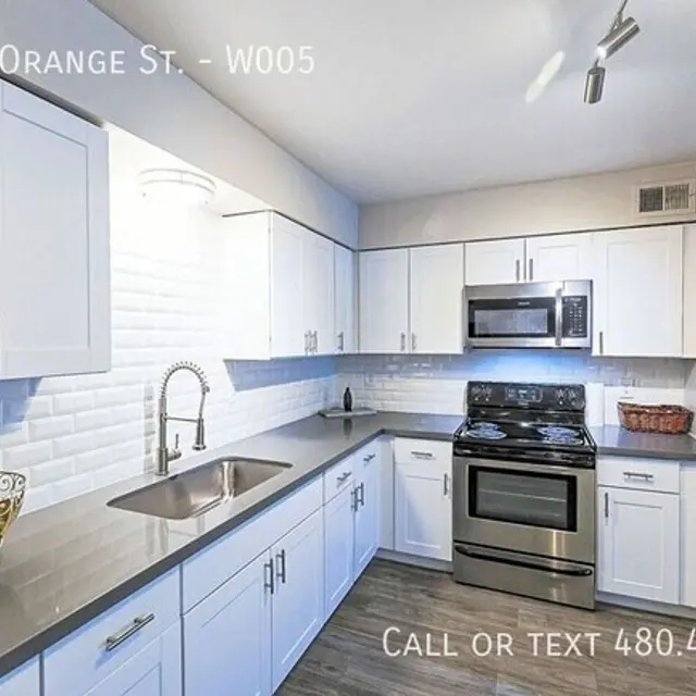 A modern kitchen featuring white cabinets, stainless steel appliances, and a gray countertop with a sink. The kitchen includes a decorative bowl and has bright, even lighting.