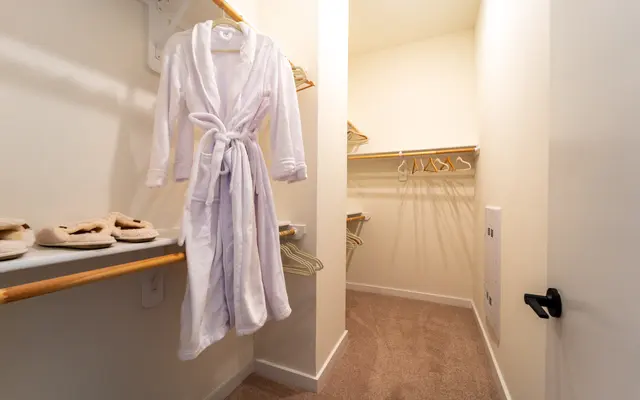 A cozy walk-in closet with a white bathrobe hanging on a rack and plush slippers on the floor.