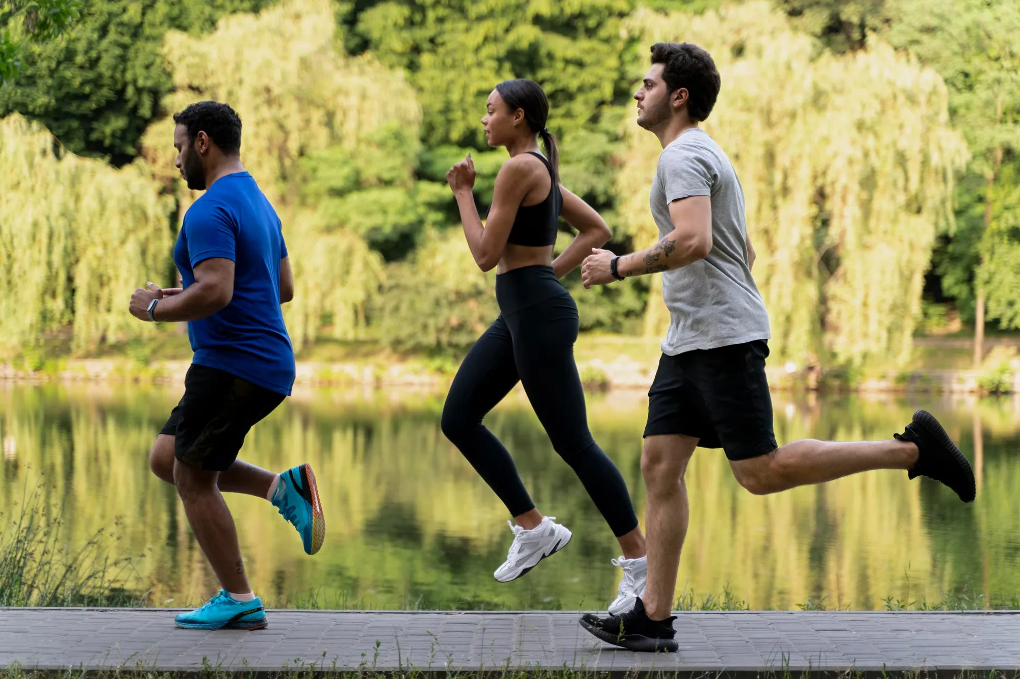 Enjoying a Run in Nature A group of three people jogging along a wooden path by a serene body of water surrounded by lush greenery.