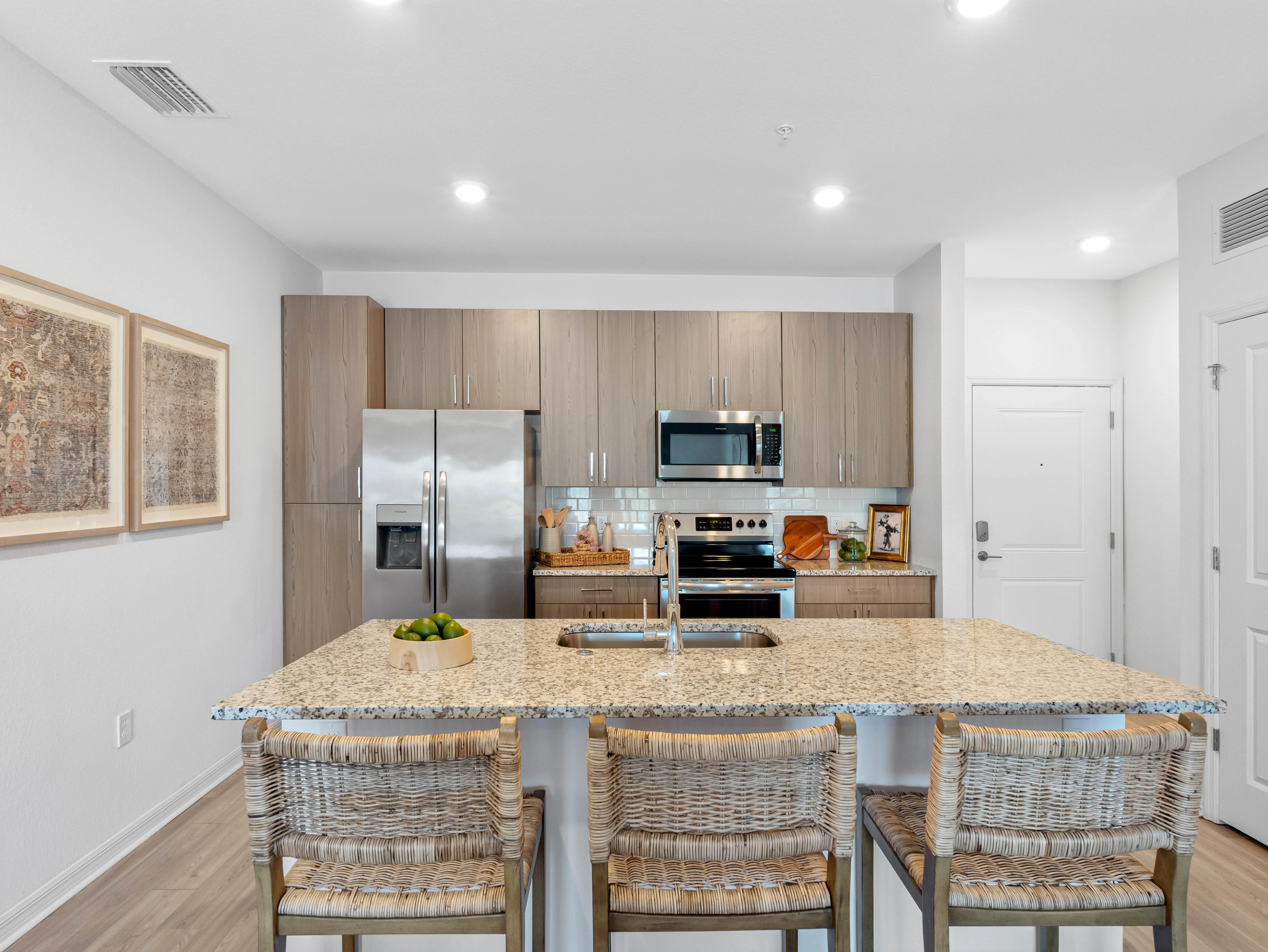 Contemporary Kitchen Interior A modern kitchen featuring a large island with four wicker bar stools, stainless steel appliances, and light wood cabinets.