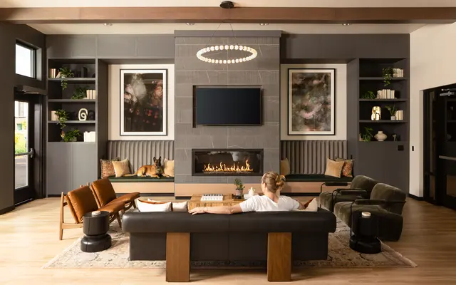 Cozy Modern Living Room A modern living room featuring a cozy arrangement with a large couch, armchairs, and a fireplace. The room has large windows allowing natural light, and decorative shelves with plants and artwork.