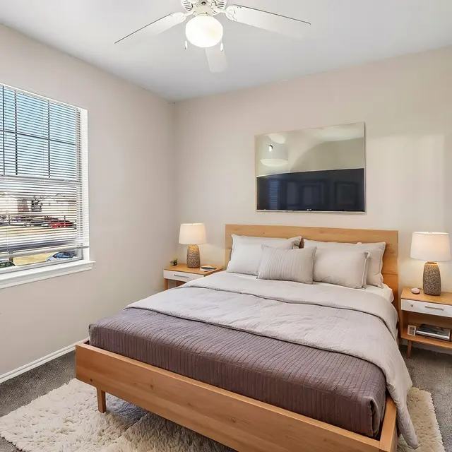 Stylish Modern Bedroom A cozy bedroom featuring a wooden bed frame, large windows, and modern decor including lamps, a plant, and a wall-mounted TV.