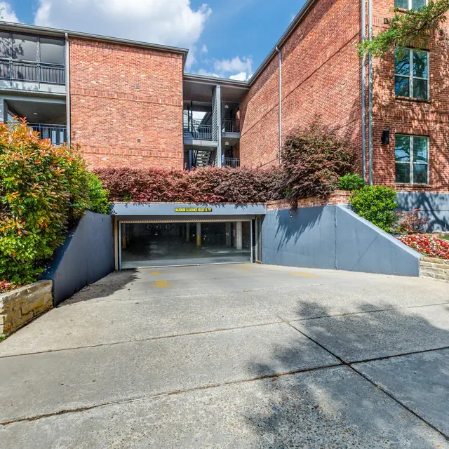 Exterior view of an apartment complex featuring a garage entrance and landscaped areas with flowers and greenery.