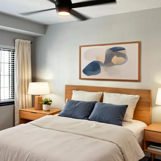 A modern bedroom featuring a double bed with white bedding and blue accent pillows, two bedside tables with lamps, a plant, and abstract wall art.