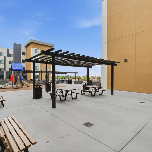 Outdoor courtyard featuring a pergola, picnic tables, and playground equipment.
