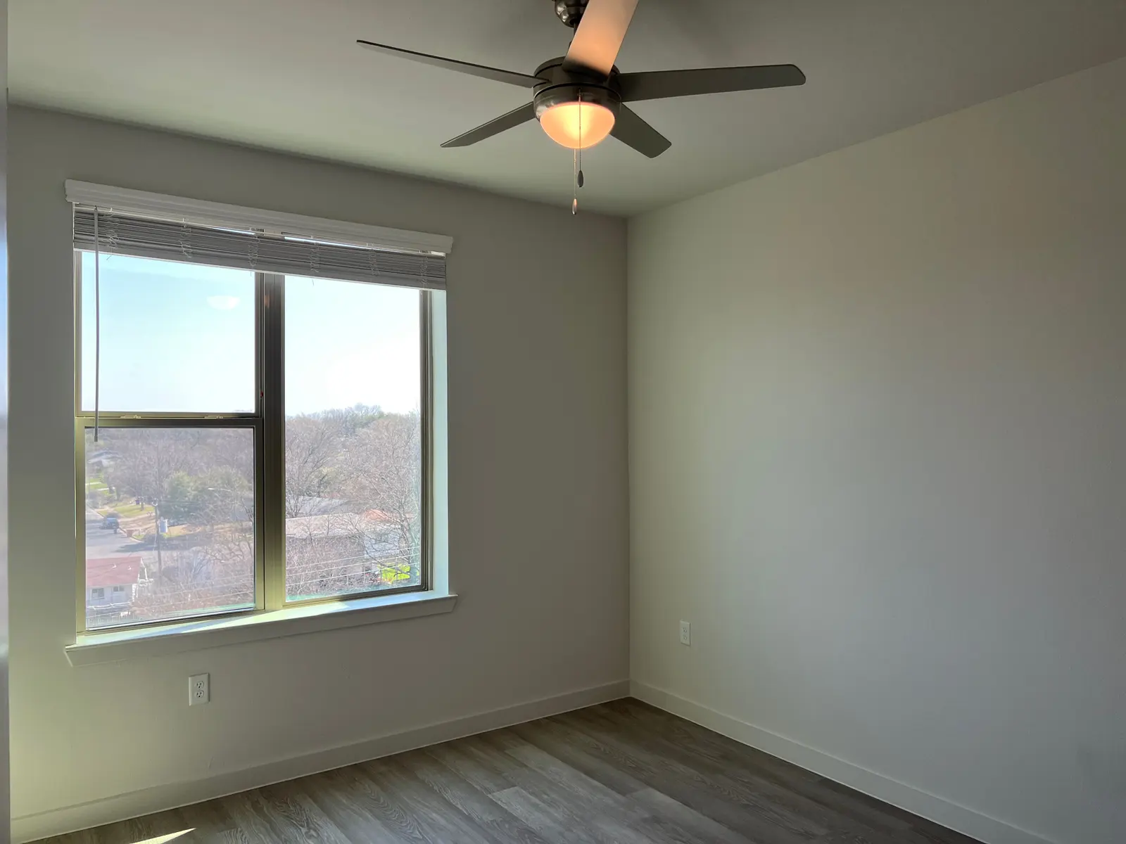 An empty room featuring a ceiling fan and a large window with a view of a neighborhood outside.