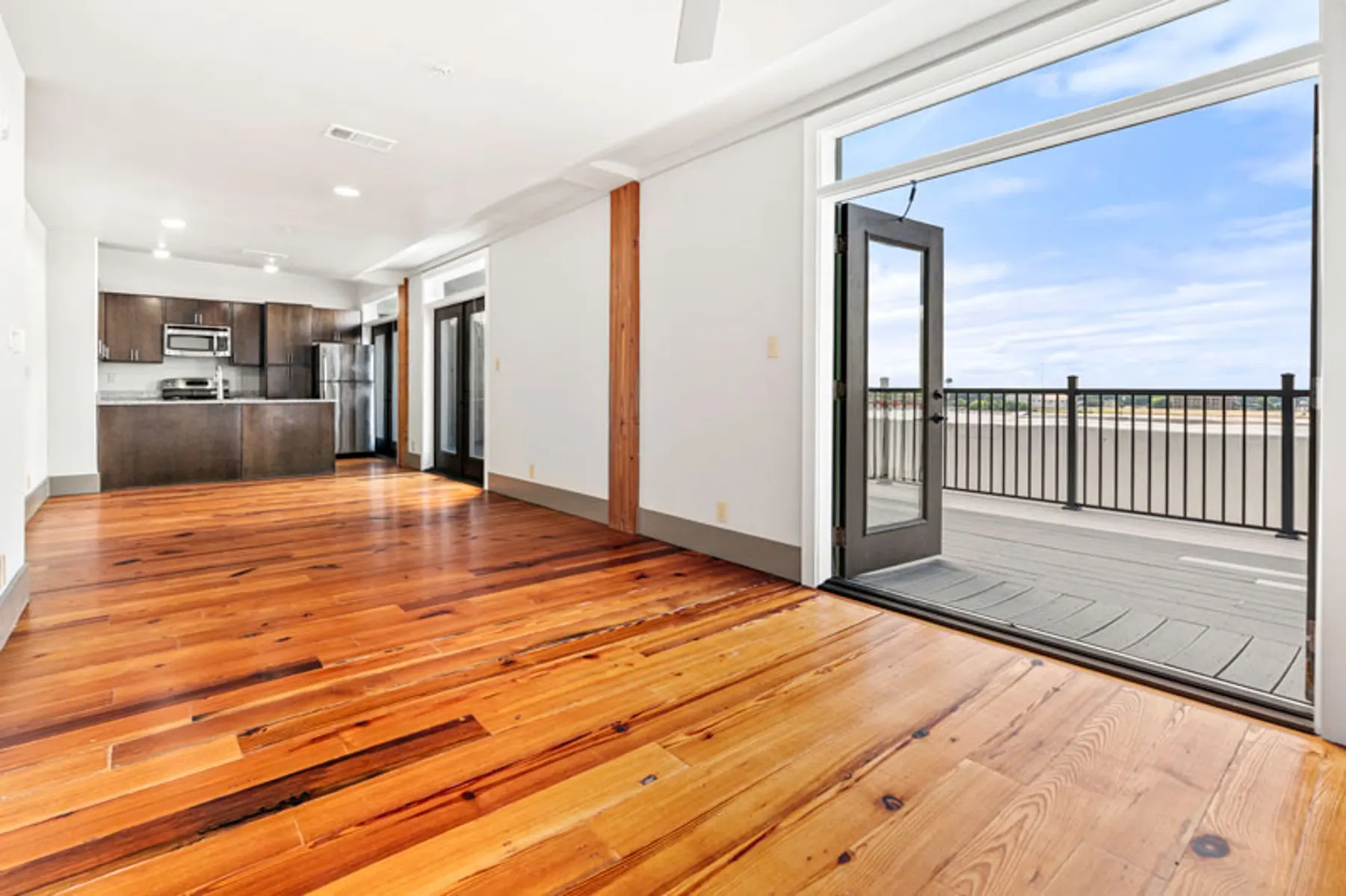 A spacious living area with hardwood floors, an open kitchen featuring modern appliances, and large doors leading to a balcony with outdoor views.