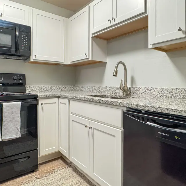 A modern kitchen featuring black appliances, white cabinets, and a granite countertop.