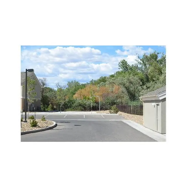 A view of an empty parking lot surrounded by greenery and trees under a partly cloudy sky.
