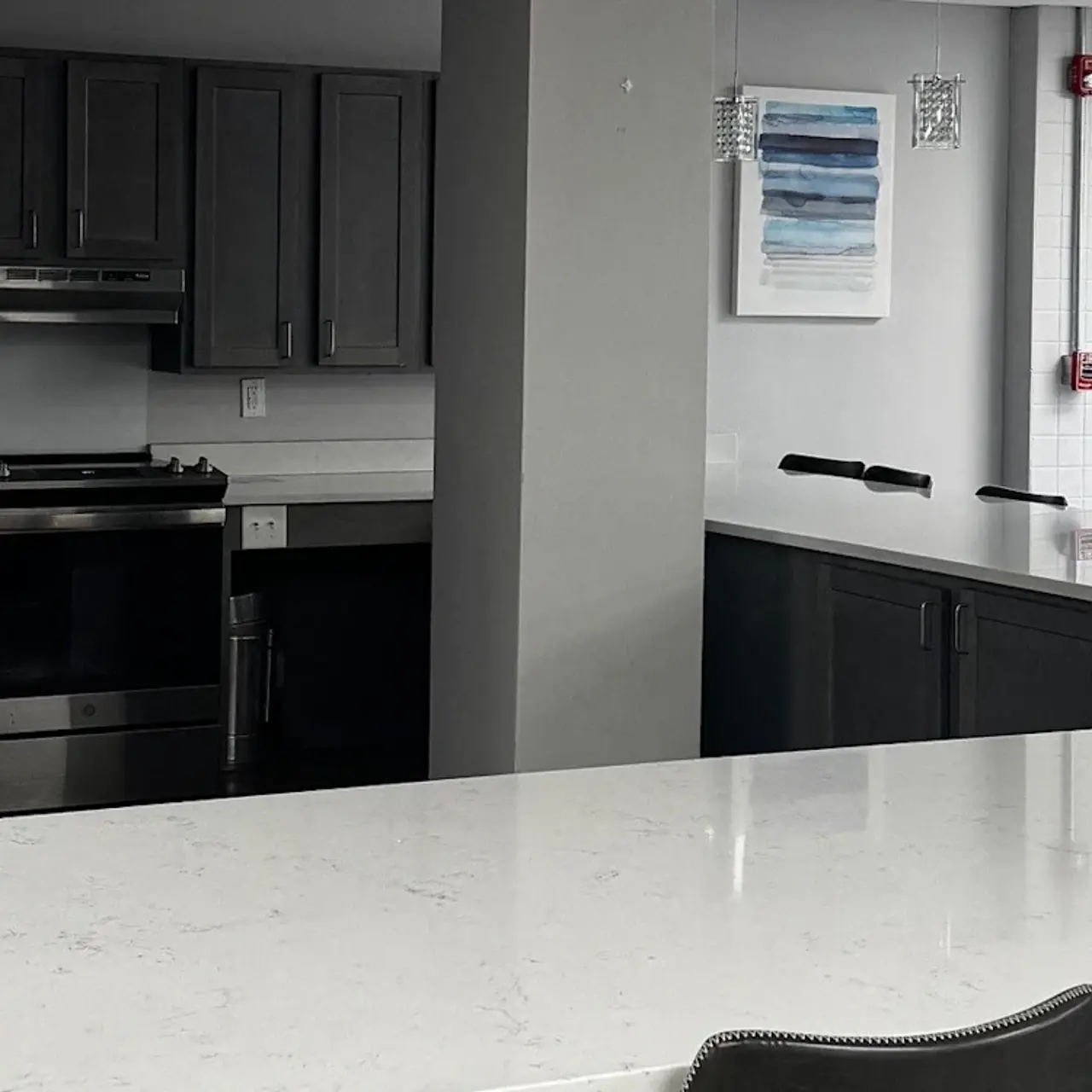 A modern kitchen with gray cabinets, stainless steel appliances, and a spacious white countertop with stools.