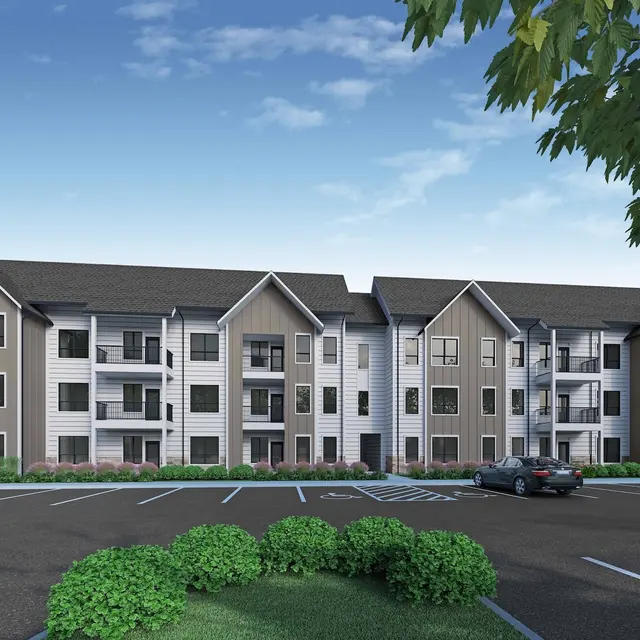 A modern three-story apartment building with a mix of wood and siding exteriors, surrounded by greenery and a parking lot.