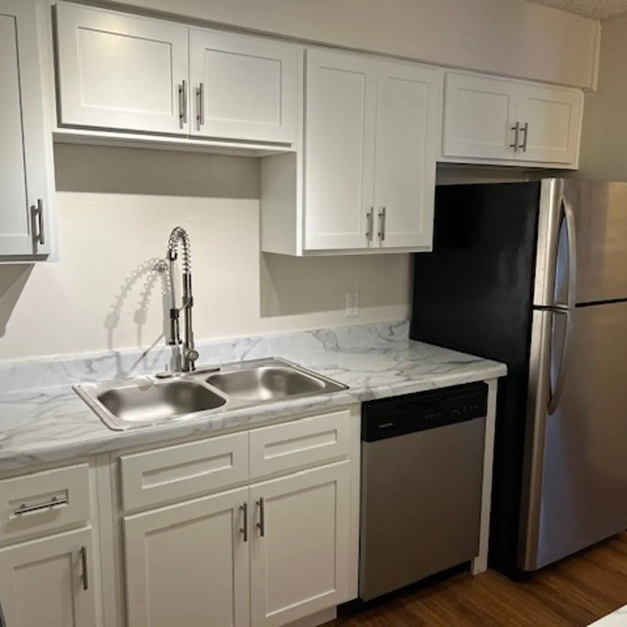 Modern Kitchen with Marble Countertop A modern kitchen featuring white cabinetry, a double sink, and stainless steel appliances including a refrigerator and dishwasher. The countertop has a marble finish with a light wood floor visible in the image.