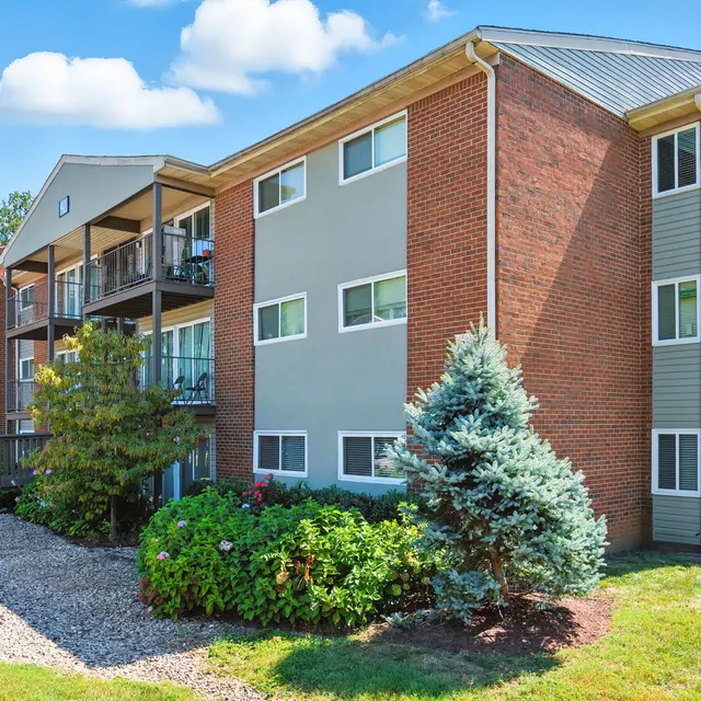 Exterior view of a modern multi-unit apartment building with a mix of brick and siding, surrounded by greenery and blue sky.