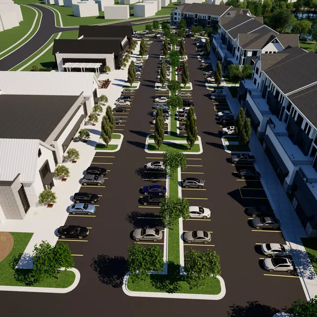 Aerial view of a modern shopping complex with rows of parked cars and surrounding greenery.