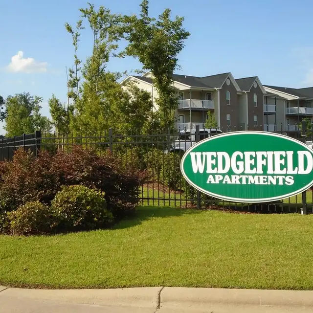 Wedgefield Apartments Entrance Sign for Wedgefield Apartments with surrounding greenery and residential buildings in the background.