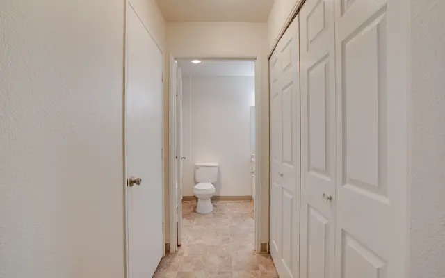A hallway with white walls and several closed doors on either side leading to a bathroom at the end.