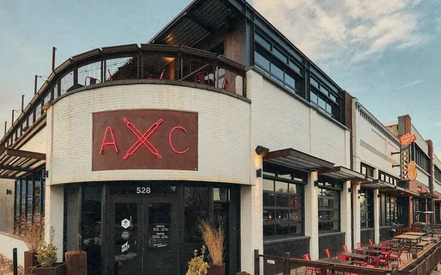 Exterior view of a modern restaurant with a neon sign and outdoor seating.