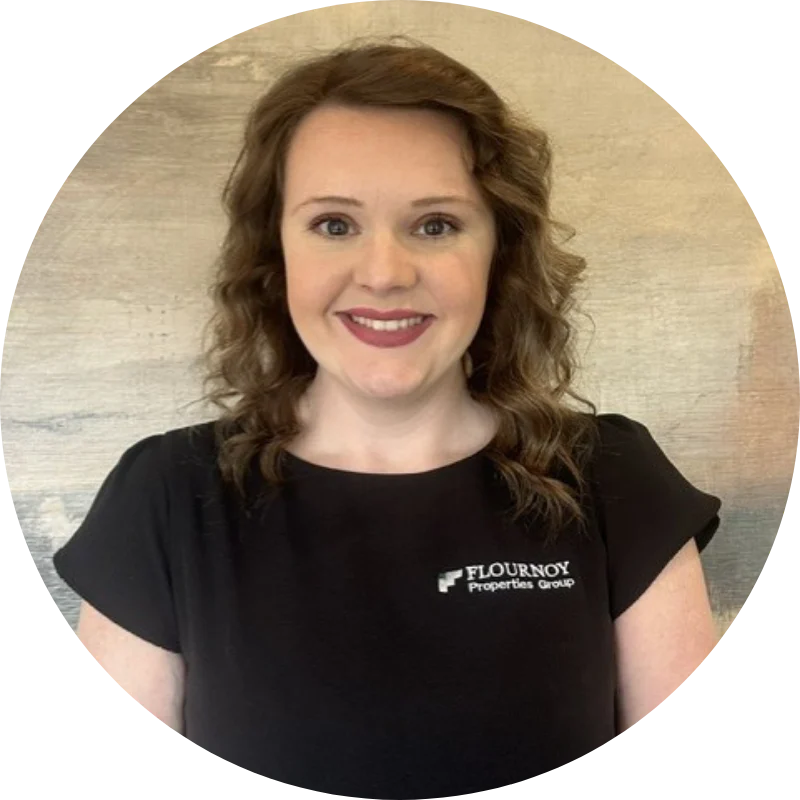 Professional Headshot for Flournoy Properties Group A woman with curly brown hair smiling at the camera, wearing a black shirt with 'Flournoy Properties Group' logo, set against a neutral background.