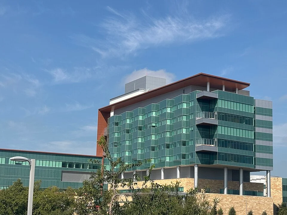 A modern office building with a combination of green glass and stone exterior, featuring multiple balconies and a unique architectural design under a clear blue sky.
