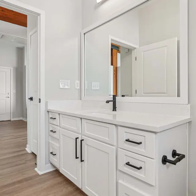 Contemporary Bathroom Design A modern bathroom featuring a double vanity with white cabinets, a large mirror, and a stylish black faucet. The floor is finished with light-colored wood, and there's a toilet in the corner. The room has neutral walls and a light atmosphere.