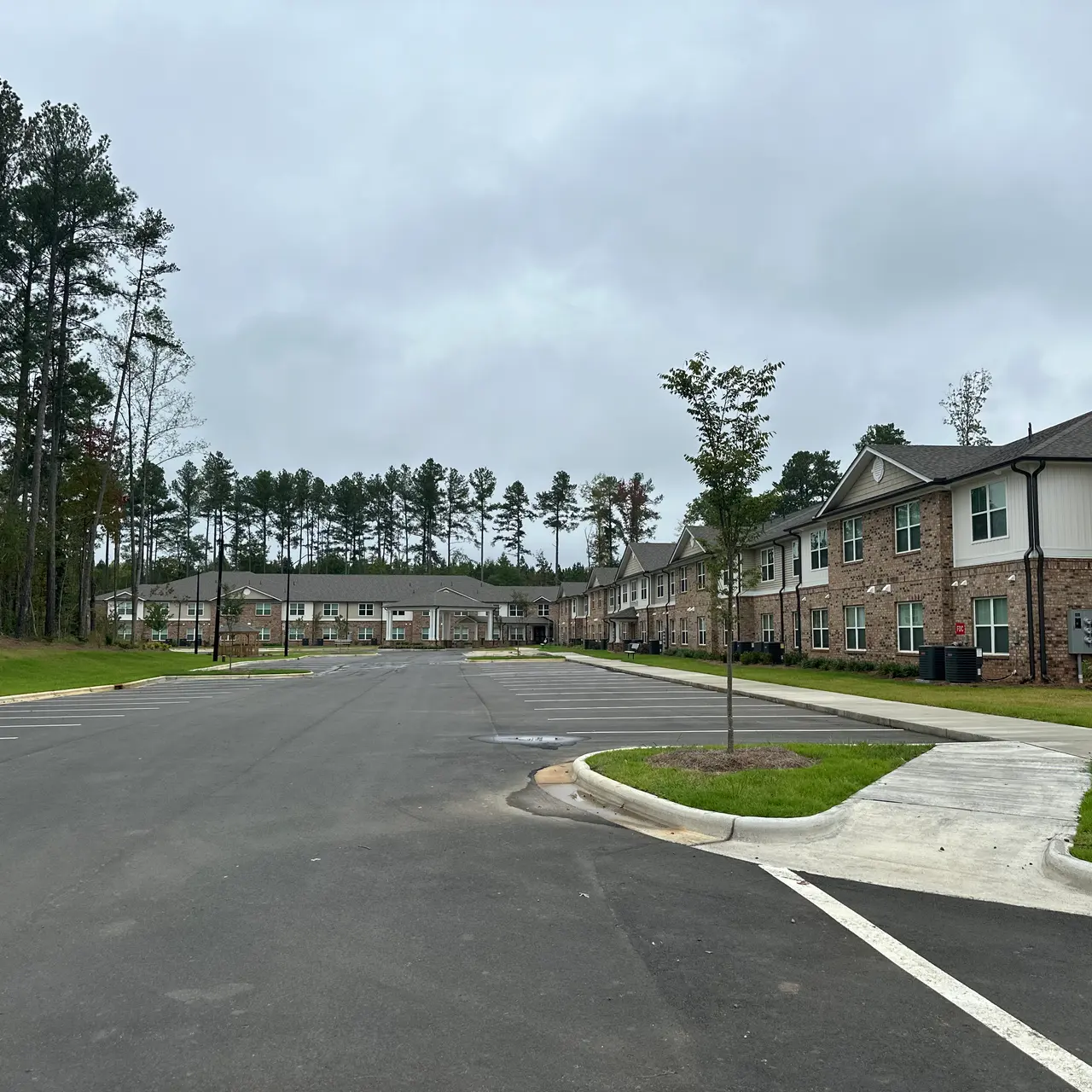 A view of a residential complex under overcast skies, featuring a brick building and a well-paved road.