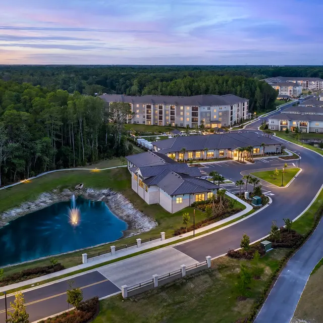 Aerial View of Modern Apartment Complex Aerial view of a modern apartment complex surrounded by trees and a pond with a fountain.