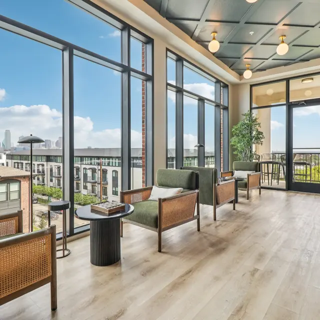 A modern lounge area featuring large windows with city views, stylish seating arrangements, and wooden flooring.