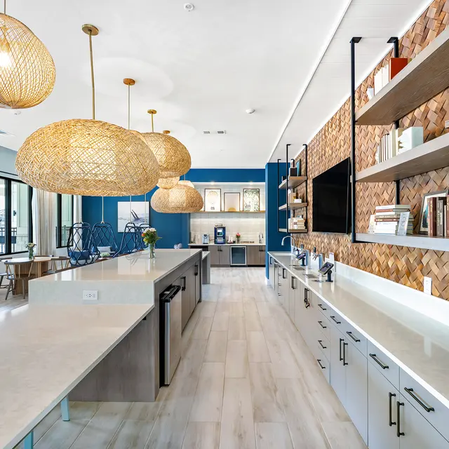 Modern Kitchen Design A modern kitchen featuring a large island with gray cabinetry, a blue accent wall, and oversized woven pendant lights. There are open shelves displaying books and decor, and a small dining area visible in the background.