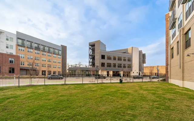 A modern building complex featuring a green lawn in the foreground and contemporary architecture in the background with a cloudy sky.