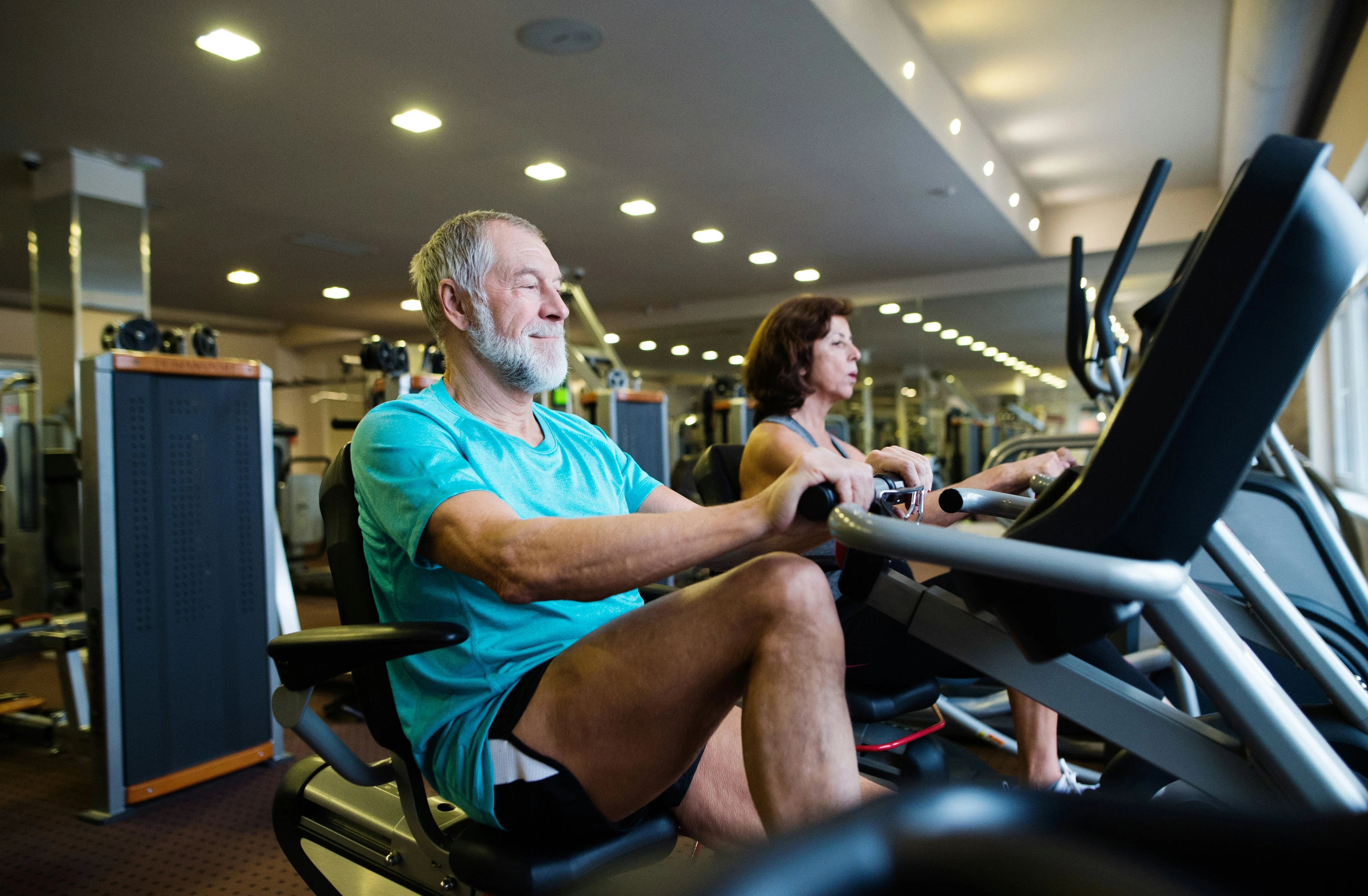 Fitness for Seniors at the Gym Two individuals exercising on machines at a gym, focusing on their fitness routines.