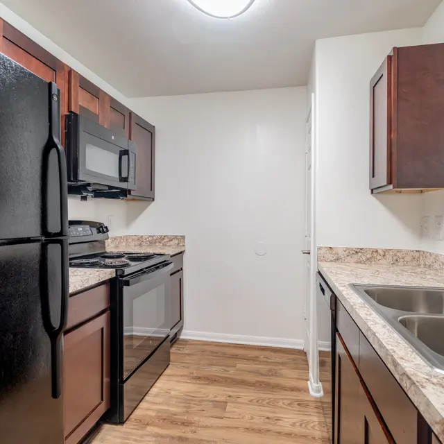 A modern kitchen featuring dark wooden cabinets and stainless steel appliances including a stove, microwave, and refrigerator, along with a double sink and granite countertops.