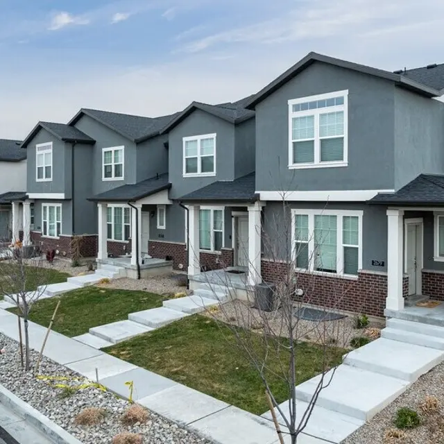 Row of modern townhouses with grey and brick exteriors, concrete pathways, and landscaped front yards.
