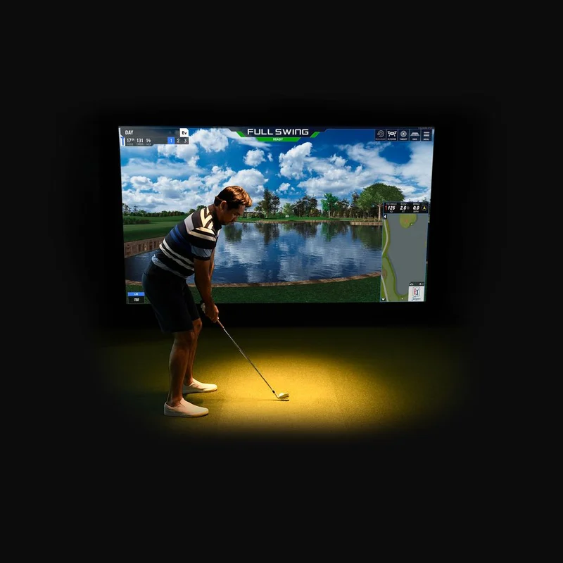 Golf Simulator Practice Session A golfer preparing to take a shot in front of a golf simulator screen showing a scenic course with a body of water and blue sky.