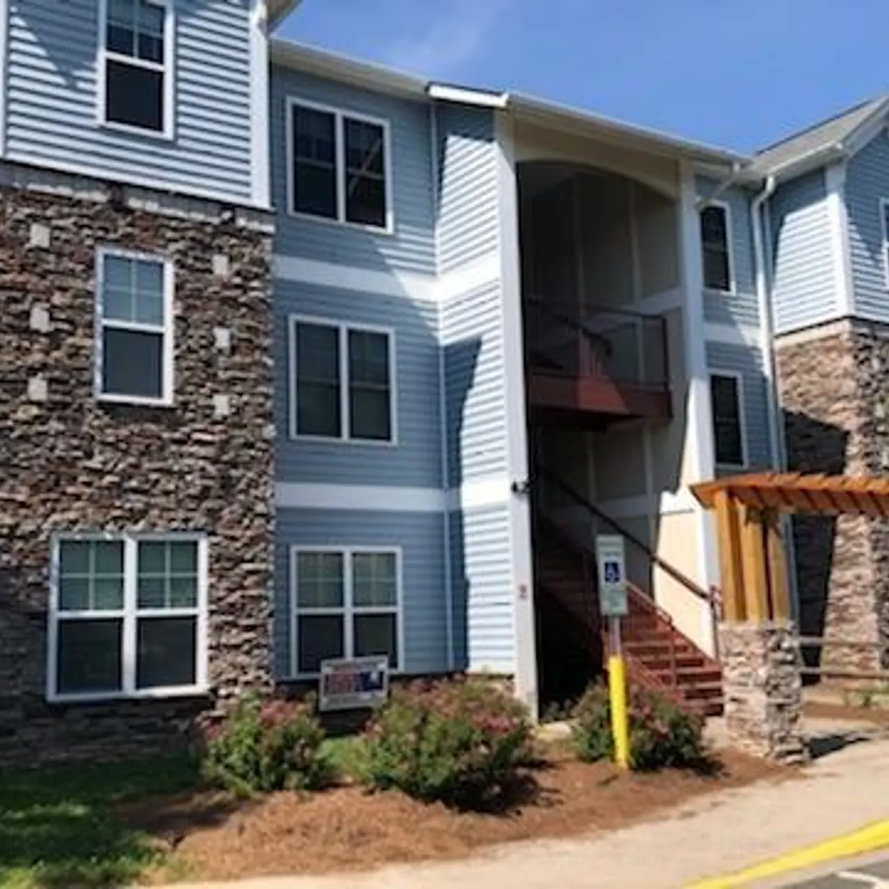 Exterior view of a three-story apartment building with stone accents and a landscaped entrance.