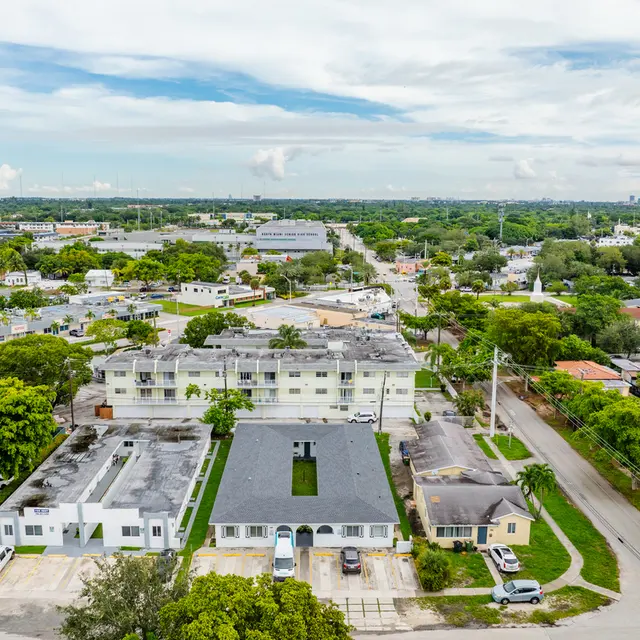 Aerial view of a suburban area featuring residential buildings, tree-lined streets, and open green spaces.