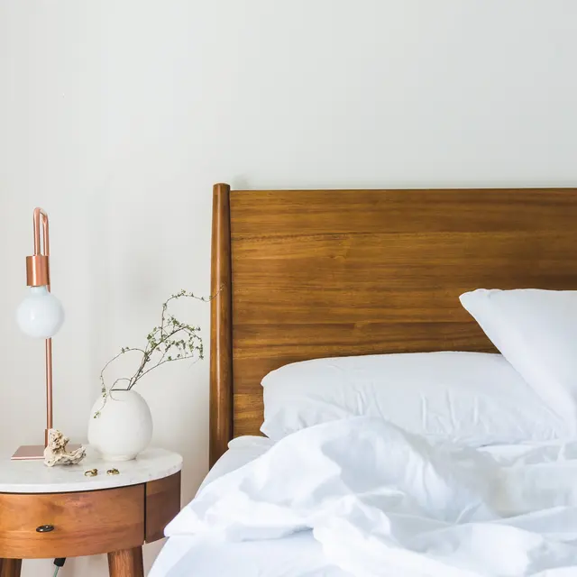 Cozy Modern Bedroom A cozy bedroom featuring a wooden bed frame, white bedding, and a bedside table with decorative items and a lamp.