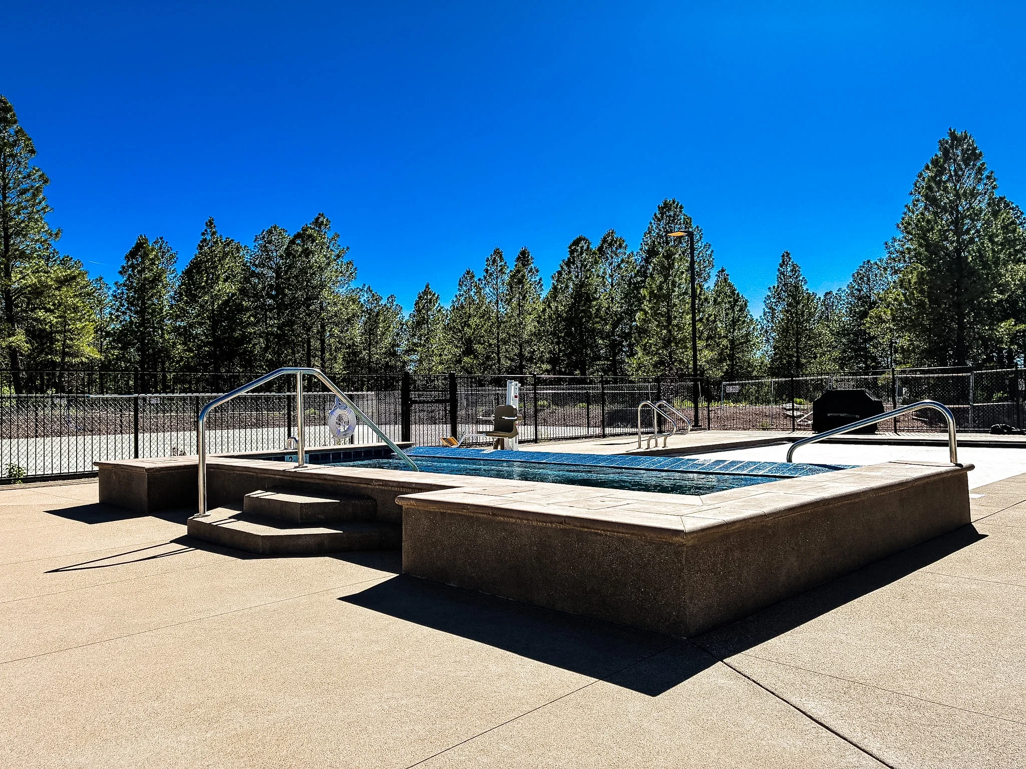 A well-maintained pool area surrounded by trees and a clear blue sky.