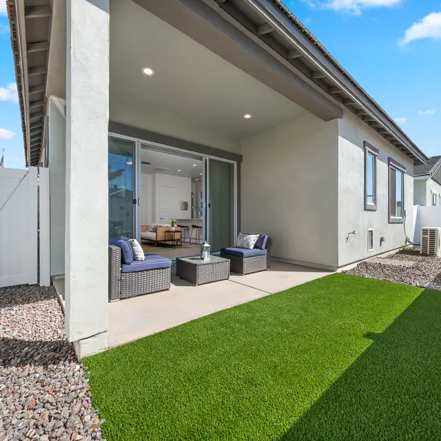 Contemporary Outdoor Patio A modern outdoor patio area featuring artificial grass, a small seating arrangement, and a view of a light-colored wall and fence.