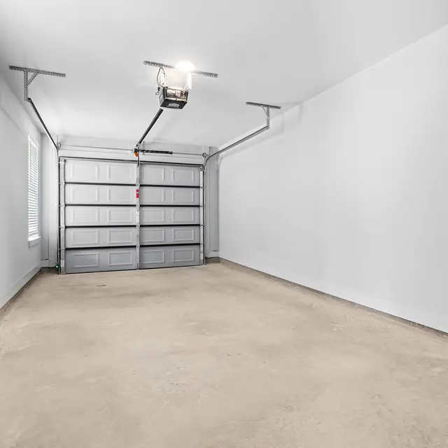 Empty Garage Interior A spacious and empty garage interior with a concrete floor and a garage door in the background. White walls and a single light fixture illuminate the space.