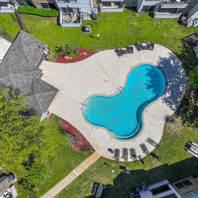Aerial view of a swimming pool shaped like a figure eight surrounded by a concrete deck, lounge chairs, and greenery.