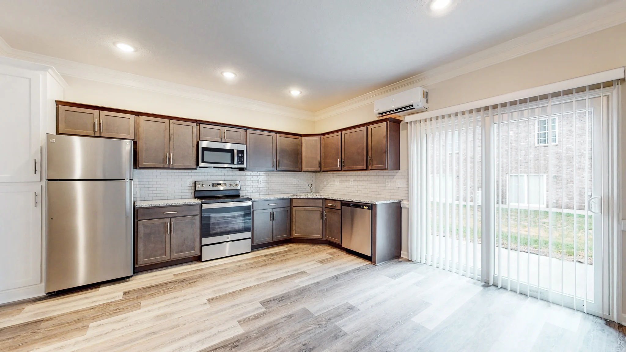 A modern kitchen featuring dark wood cabinets, stainless steel appliances, and a sliding glass door leading to an outdoor area.