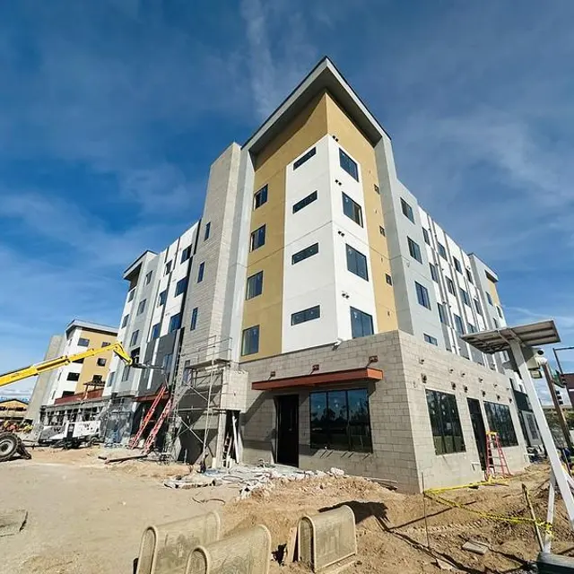 A multi-story building under construction with a modern design featuring beige and white panels, surrounded by construction equipment and materials.