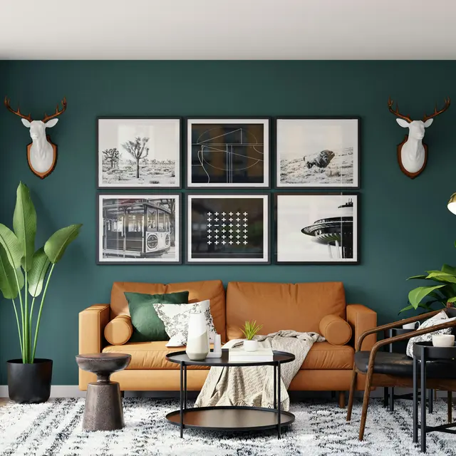 A modern living room featuring a brown sofa, a round coffee table, and various indoor plants. The wall behind is dark green with framed artworks and decorative animal heads mounted on it. Large windows allow natural light to fill the space, contrasting with the light wood flooring and patterned rug.