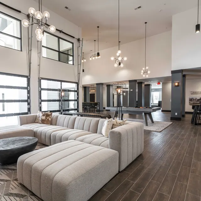A spacious modern living room featuring a large sectional sofa, a round coffee table, and stylish lighting fixtures. Large windows provide natural light.