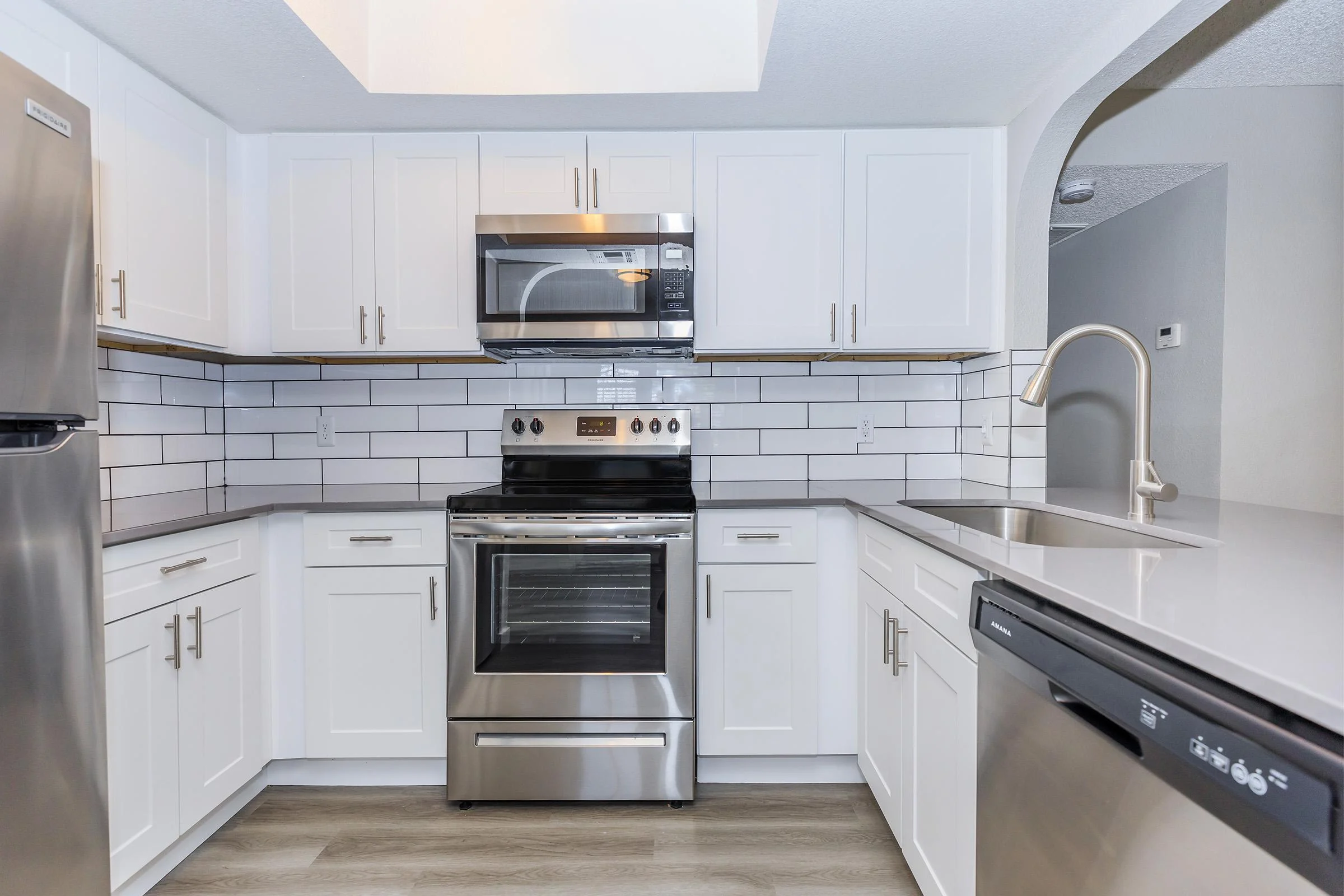 Modern Kitchen Design A modern kitchen featuring white cabinetry, stainless steel appliances, and a tile backsplash. The kitchen has a spacious layout with a stove, microwave, and a sink with a contemporary faucet.