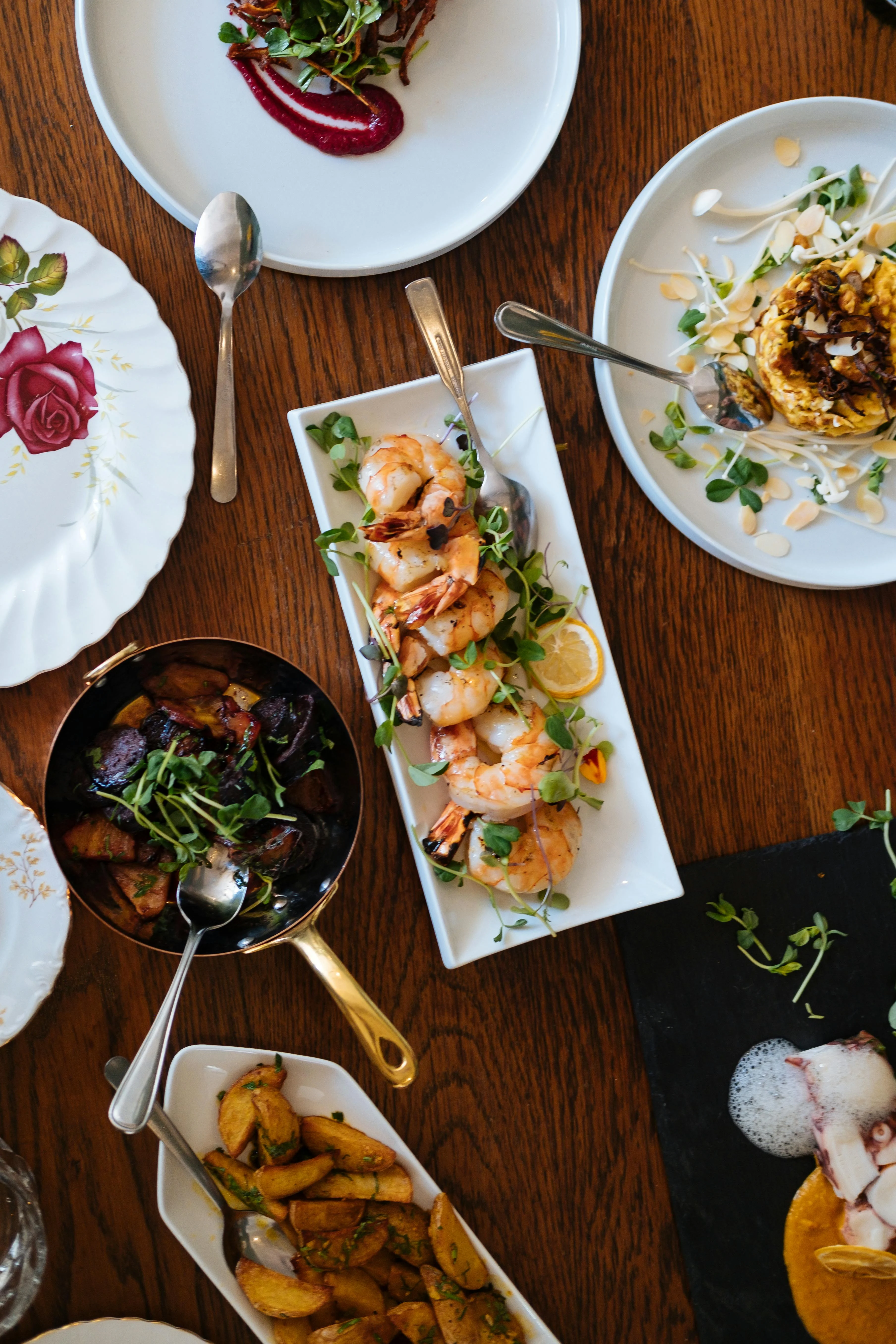 A variety of gourmet dishes including grilled shrimp, colorful sauces, and side items on a wooden table.