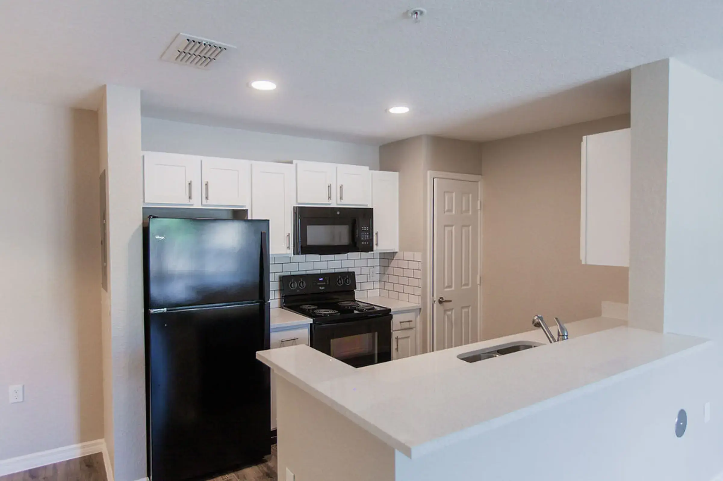 A modern kitchen layout featuring white cabinets, a black refrigerator, a black stove, and a microwave, with a countertop that separates the kitchen from the living area.