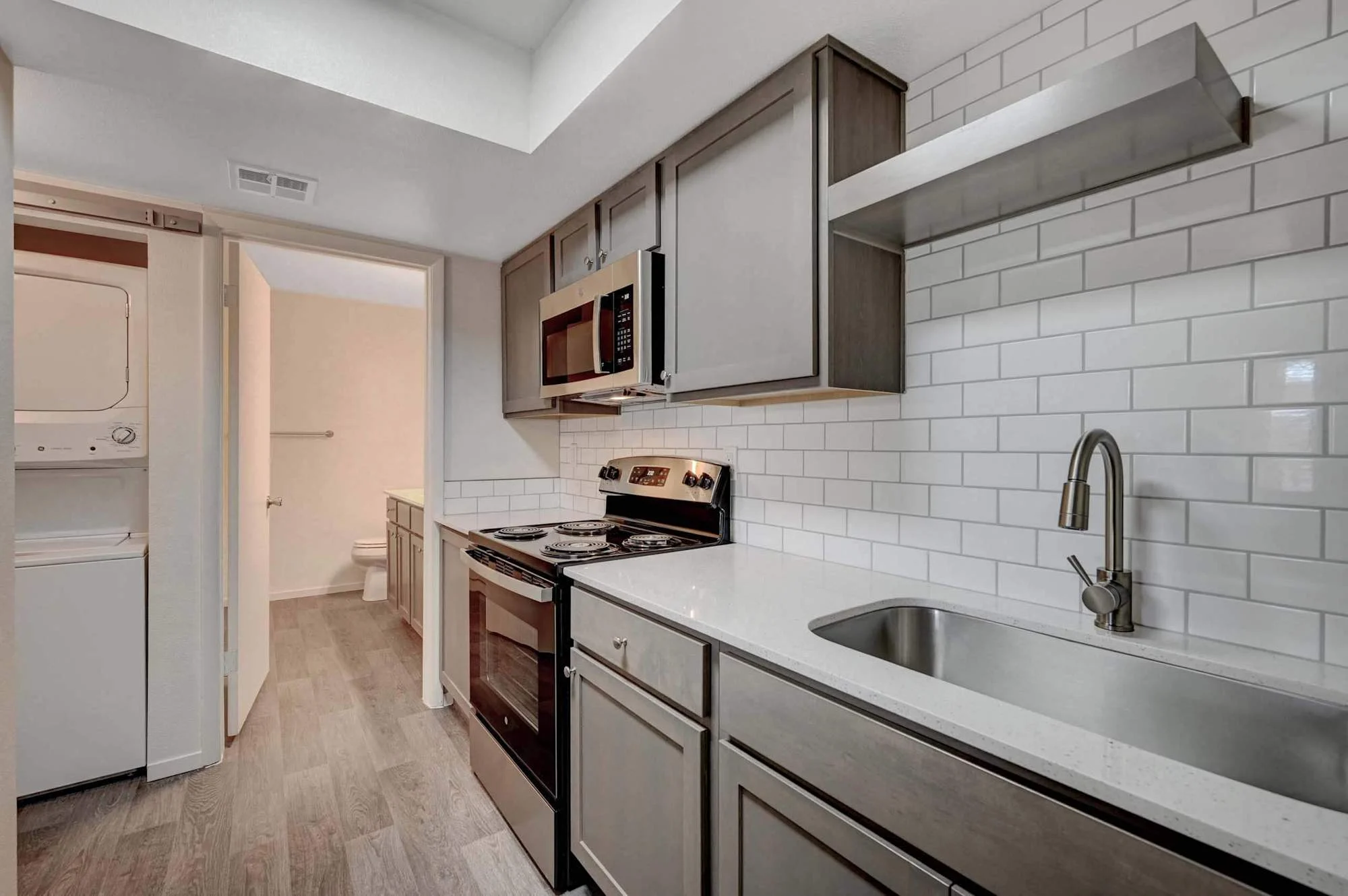 Modern Kitchen with Stainless Steel Finishes A modern kitchen featuring stainless steel appliances, white subway tile backsplash, and wooden flooring. The kitchen includes an oven, microwave, and sink with a sleek faucet.