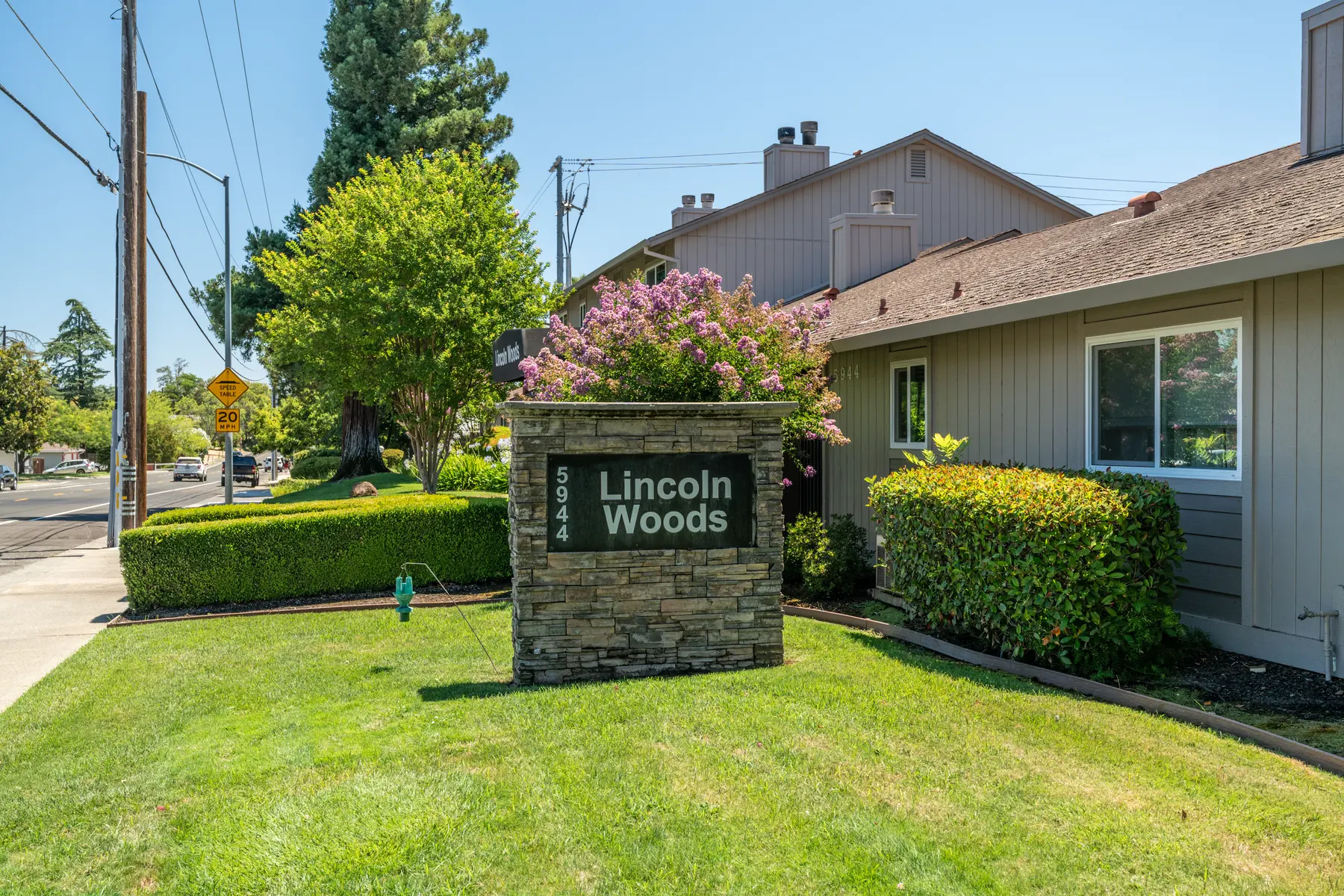 Sign displaying 'Lincoln Woods' in front of a landscaped area with trees and bushes.